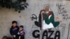 Displaced Palestinian children stand next to a mural painting by artist Amal Abo in Rafah in the southern of Gaza Strip, on Dec. 31, 2023.