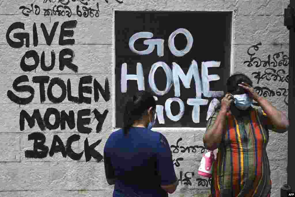 Women stand in front of a graffiti painted outside the premises of Sri Lanka&#39;s presidential palace, in Colombo, a day after it was overrun by anti-government protesters.