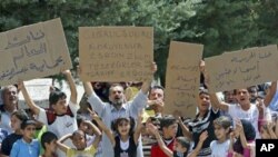 Penaberên Sûrî bi pankartên xwe dixwazin dengên xwe bilind bikin. Pankarta duyê ya ji destê rastê dibêje "Cisr El Shugur ji Beşar Esed bipareze. Spas ji Tirkîyê re, spas ji Erdogan re". Bajarokê Kampa Penaberan ya Altinozu'yê. Hatay, Tirkîye.