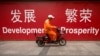 FILE - A maintenance worker rides a scooter past banners reading "Development" and "Prosperity" in English and Chinese on a street in central Beijing, July 15, 2015.